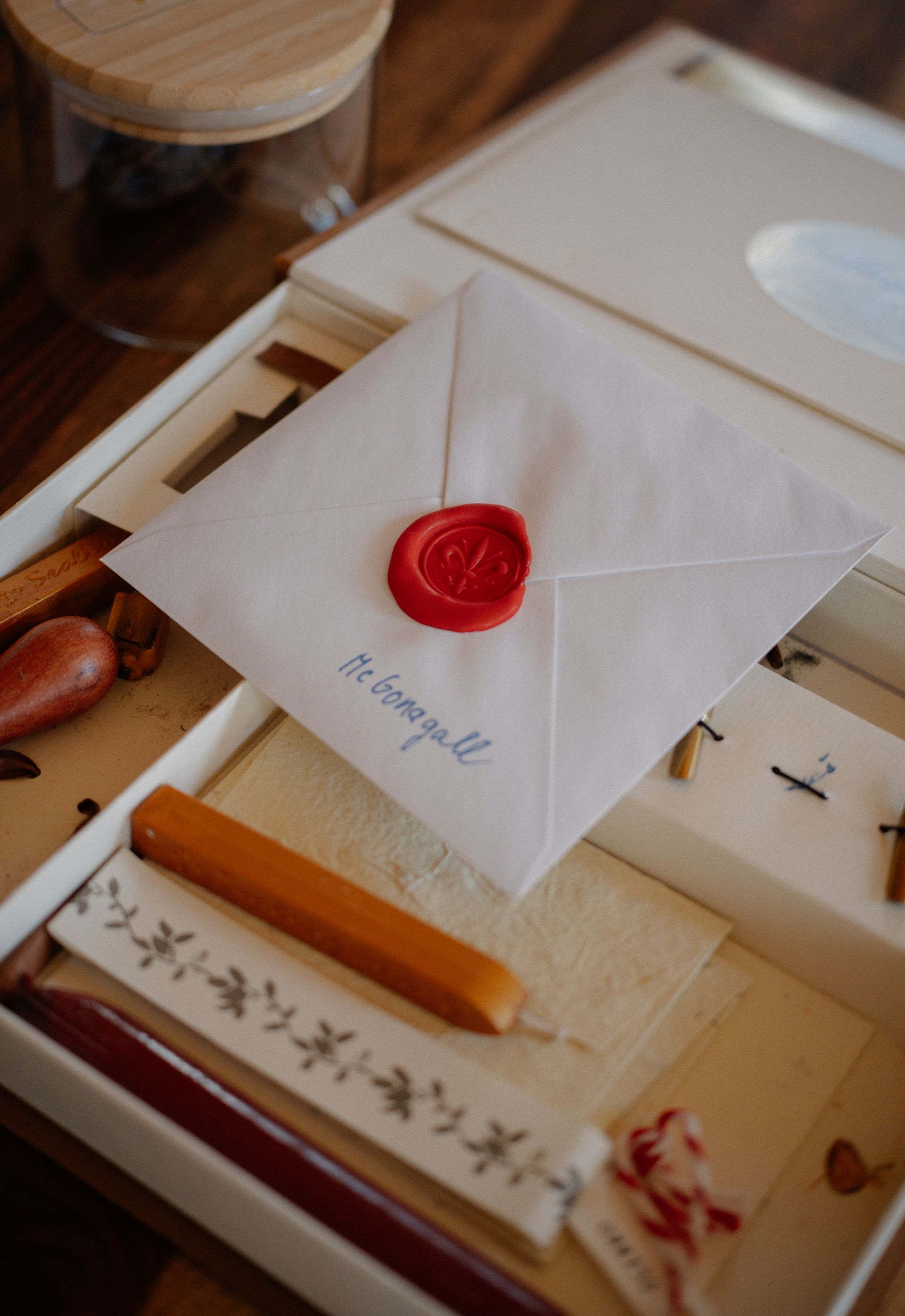 A sealed envelope with a red wax seal resting beside a wax stick and botanical stationery in a wooden desk drawer